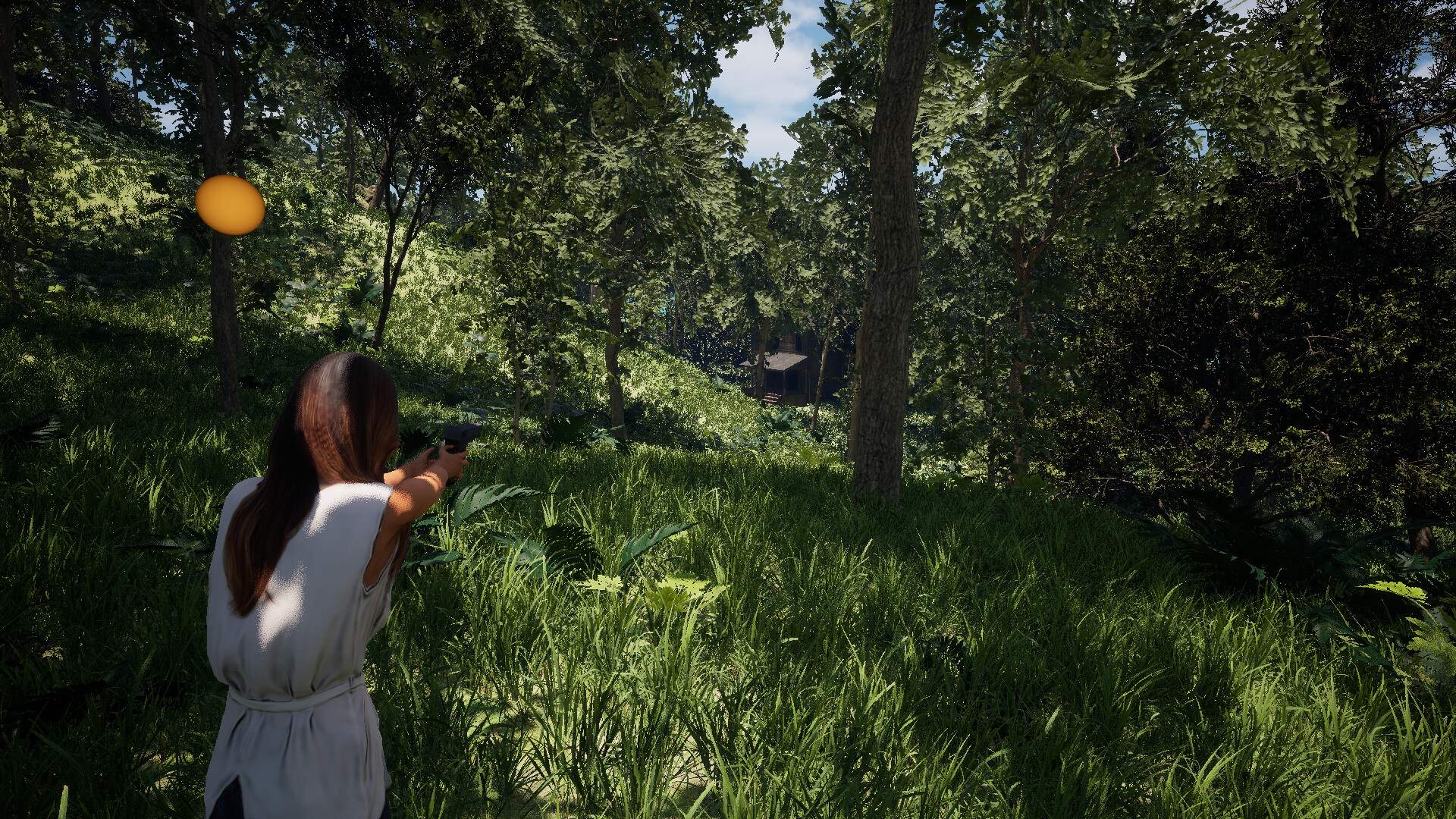 The image shows a person with long brown hair wearing a white sleeveless top and holding a handgun with both hands, aiming forward in a dense forest setting. The person is standing on a lush, green grassy area surrounded by tall trees with thick foliage, allowing sunlight to filter through and create dappled shadows on the ground. In the distance, partially obscured by the trees, there is a small wooden cabin or structure visible on a slight hill.
