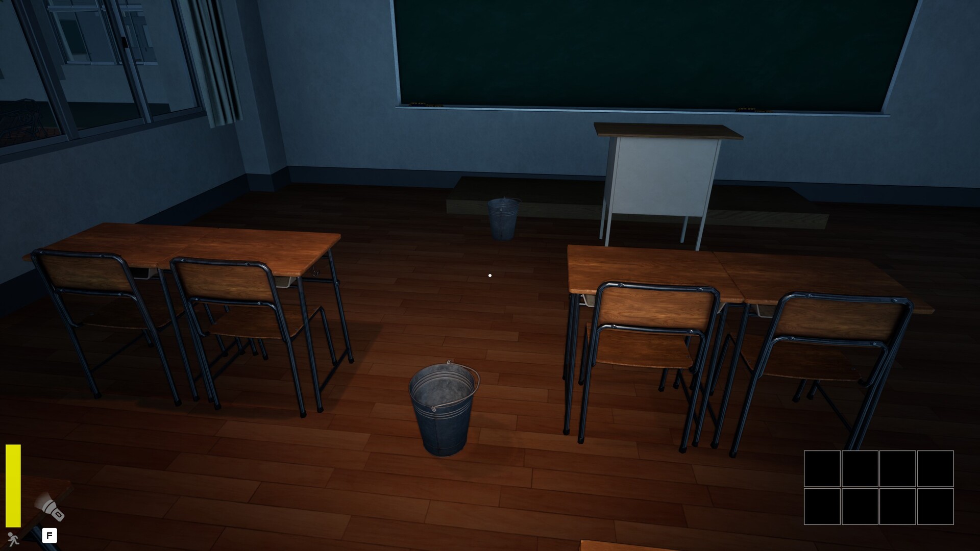 The image shows a dimly lit classroom with wooden floors and two sets of wooden desks and chairs arranged in pairs. In the center of the room, there is a metal bucket placed on the floor. At the front of the classroom, a simple teacher's podium stands in front of a large green chalkboard. The room appears quiet and empty, with some windows visible on the left side and curtains partially drawn.