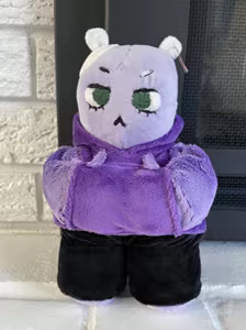 Photo of the real life plushie that is used for the main character of WEJbA; she's a purple bear in a hoodie.
